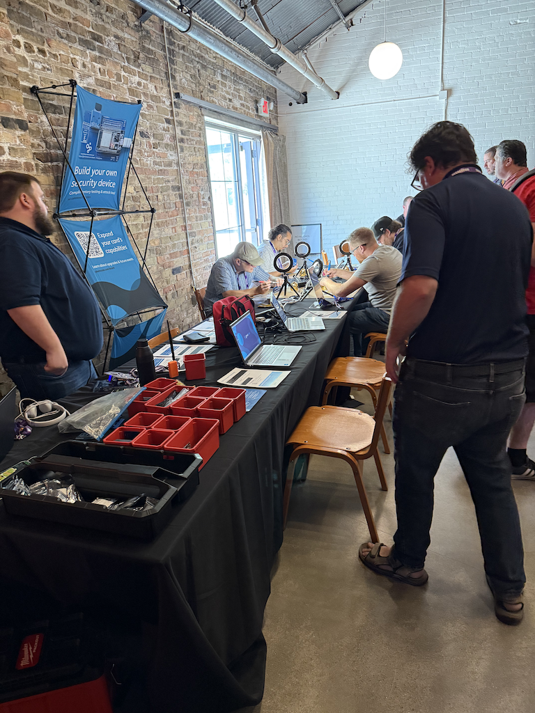 4 people are seated at a long table, all concentrating on soldering.